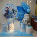 Mesa decorada com o tema do filme Frozen, painel bolo, docinhos e balões em buffet infantil