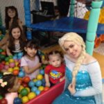 Crianças junto com pessoa vestida de Elsa, do filme Frozen em buffet infantil